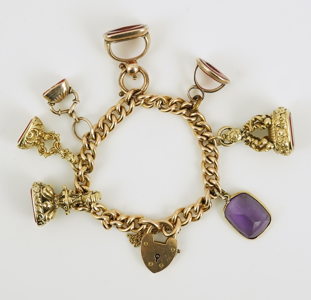 An Edwardian 15ct gold curb link charm bracelet with heart shaped padlock clasp, hung with six assorted gold overlaid and carnelian set fob seals